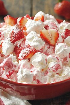 a bowl filled with strawberries and whipped cream on top of a red table cloth