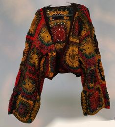 a crocheted jacket is displayed on a white surface with an orange, yellow and red pattern