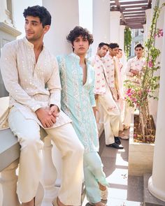 several men in white and blue outfits are sitting on the ledge outside an apartment building