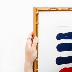 a person holding up a painting in front of a bamboo frame with red, white and blue paint on it