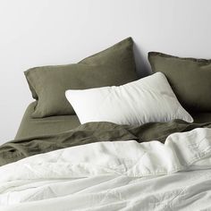 an unmade bed with white pillows and green linens on the headboard is shown