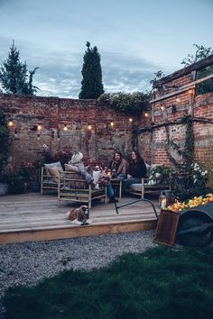 two people sitting on wooden chairs in the middle of a patio with lights strung up above them