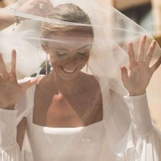 a woman wearing a white wedding dress under a veil with her hands in the air