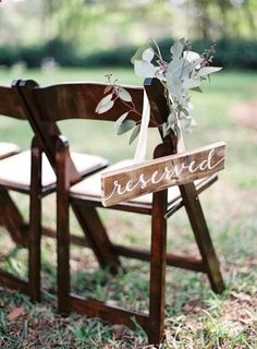 a wooden chair with a sign that says reserved on it and flowers in the back