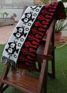 a black and red blanket sitting on top of a wooden chair next to a potted plant