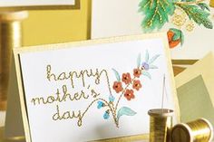 two greeting cards on a table next to some thread and spools, with the words happy mother's day written in gold