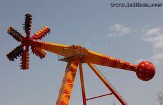 an amusement park ride with red and yellow designs on it's sides, against a blue sky