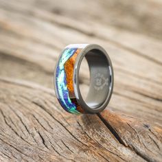 a wedding ring with an orange, blue and green pattern on it sitting on top of a wooden table