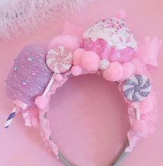 a pink and white headband with pom poms on the ears, sitting on a pink surface