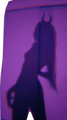 the shadow of a person standing in front of a purple wall with a devil on it