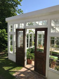 a white house with two brown doors and some potted plants on the side walk