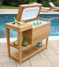 an outdoor cooler sitting on top of a wooden table next to a swimming pool with chairs around it