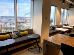 an office with couches and tables in front of large windows looking out on the city