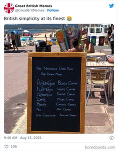 a blackboard sign sitting on the side of a road next to a table and chairs