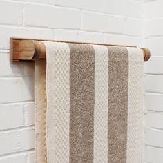 a brown and white striped towel hanging on a wooden rack next to a brick wall