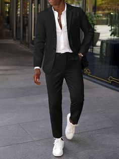 a man walking down the street wearing a suit and white shoes with his hands in his pockets