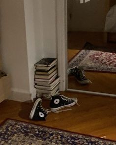 a pile of books sitting on top of a wooden floor next to a doorway with a mirror