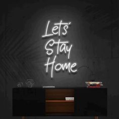 the words let's stay home are lit up against a black wall with a wooden cabinet