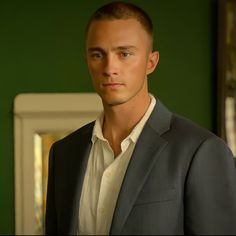 a man in a suit and white shirt looking at the camera while standing next to a green wall