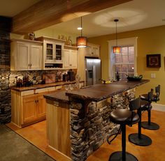 a kitchen with an island made out of stone and wooden cabinets, two bar stools in front of it