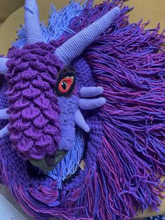 a purple knitted animal head with horns and large, long hair on it's face