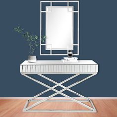 a white table with a mirror and plant on it in front of a blue wall