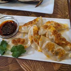 some dumplings are on a white plate with dipping sauce