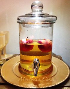 a glass jar filled with liquid sitting on top of a gold plate next to glasses