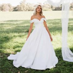 a woman wearing a white wedding dress standing in the grass with her hands on her hips