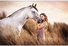 a beautiful woman standing next to a white horse in a field with tall brown grass