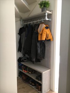 an open closet with shoes and coats hanging on the wall, next to a potted plant