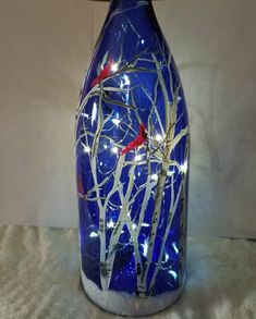 a blue glass bottle with branches and lights in the bottom is sitting on a table