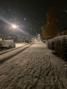 a snow covered street at night with cars parked on the side