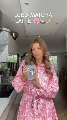 a woman in a pink dress is holding a starbucks cup and looking at the camera