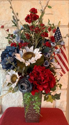 a vase filled with red, white and blue flowers on top of a table next to an american flag