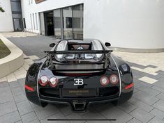 a black sports car is parked in front of a building with its hood up and the top down