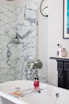 a bathroom with a bathtub, shower head and clock on the wall next to it