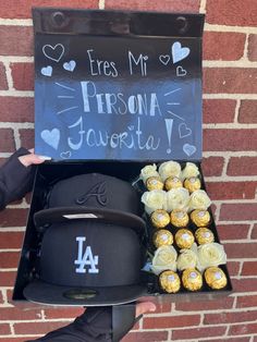 a person holding up a sign and some chocolates in a box with a baseball cap on it