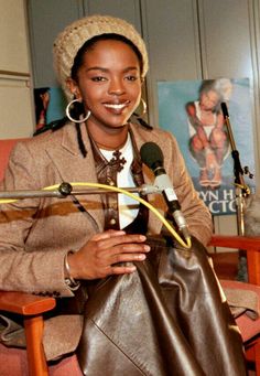 a woman sitting in a chair holding a microphone and smiling at the camera while wearing a hat