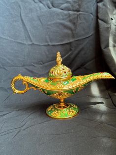 an ornate green and gold teapot on a black cloth covered table with a gray background