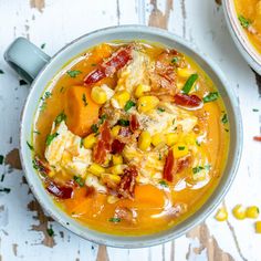 two bowls filled with soup on top of a white wooden table next to corn and carrots