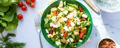 a green bowl filled with salad on top of a white table next to silverware