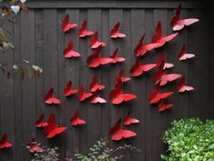 red paper birds are hanging on the side of a wooden fence in front of green plants