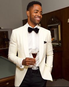 a man in a white tuxedo holding a glass of wine and smiling at the camera