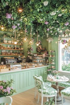 the interior of a flower shop with green walls and white tables, chairs, and shelves filled with flowers