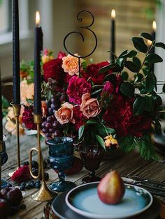 the table is set with candles, plates and vases filled with colorful flowers on it