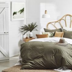 a bed with green sheets and pillows in a room next to a white wall, potted plant