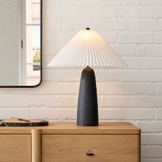 a table lamp sitting on top of a wooden dresser next to a white brick wall