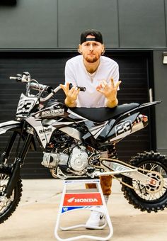 a man sitting on top of a dirt bike in front of a garage door holding his hands up