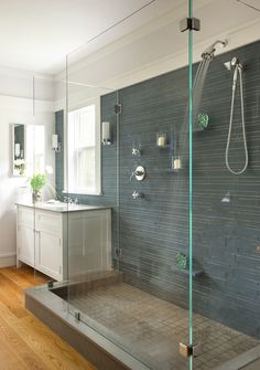 a bathroom with a walk in shower next to a white sink and wooden flooring